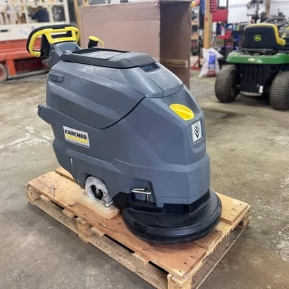 Side view of a Karcher BD 50/50 C Bp Classic walk-behind floor scrubber on a pallet in an industrial shop